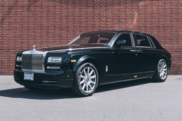 Black Rolls Royce Phantom available for rent in front of red brick wall.